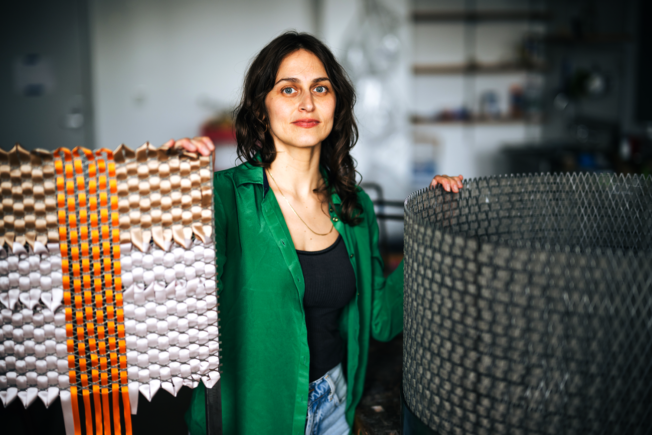Alina Tenser wears a green shirt and stands with her sculptures in a studio at Lehigh University.